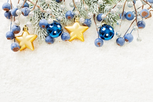 Sfondo di Natale con ramoscello di albero di Natale stelle dorate sfere di vetro blu e bacche su neve bianca