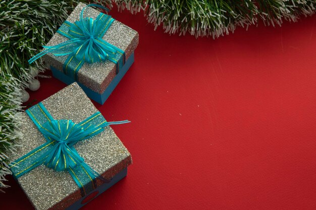 Sfondo di Natale con scatole regalo con fiocco blu, rami verdi e sfondo rosso