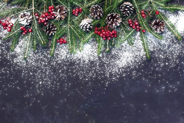 Sfondo di Natale e Capodanno, rami di abete verde e bacche rosse con neve su sfondo grigio scuro