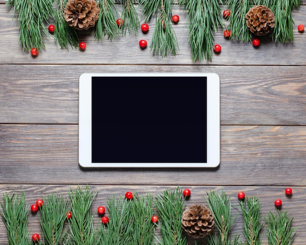 Sfondo di Natale o Capodanno su uno sfondo di legno. Tablet con uno schermo vuoto per i saluti. Lay piatto, vista dall'alto, copia spazio.