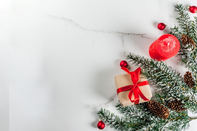 Sfondo di Natale per auguri. Rami di albero di Natale con effetto neve con nastro rosso festivo, pigne, scatole regalo e candele, su sfondo di marmo bianco