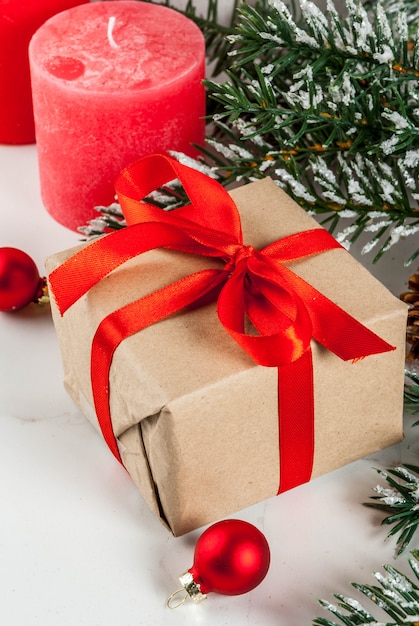 Sfondo di Natale per auguri. Rami di albero di Natale con effetto neve con nastro rosso festivo, pigne, scatole regalo e candele, su sfondo di marmo bianco