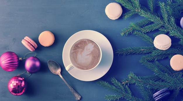 Sfondo di Natale - Tazza di cappuccino con torta, macarons, giocattoli di Natale e rami di alberi