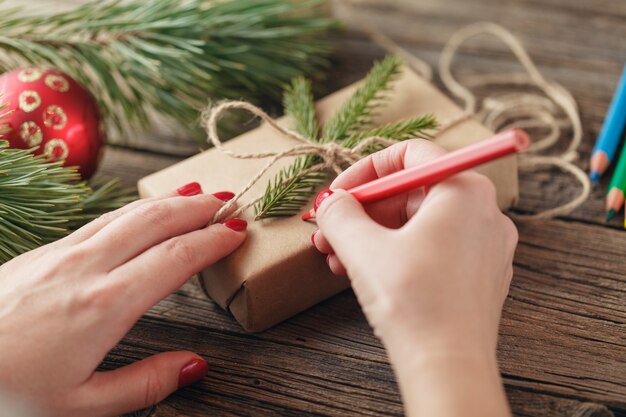 Sfondo di natale. vista delle mani che scrivono sulla confezione regalo. Regali e pergamene confezionati, rami di abete rosso sul tavolo di legno squallido. Luogo di lavoro per la preparazione di decorazioni fatte a mano di Capodanno.