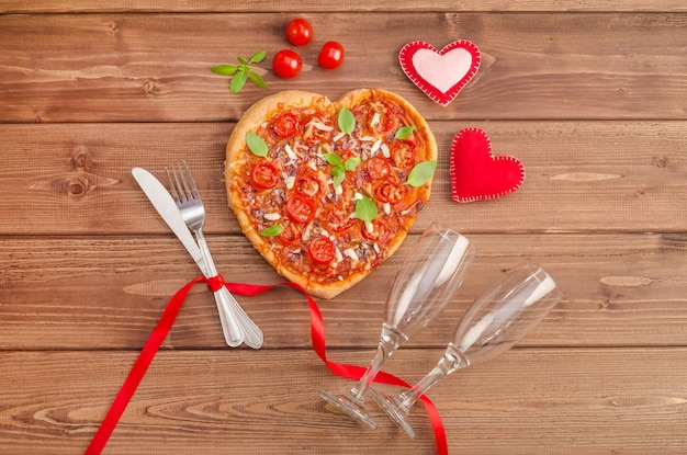 Sfondo di San Valentino con cuore di pizza e bicchieri di vino su uno sfondo di legno scuro, piatto