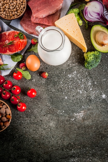 Sfondo dieta sana. Ingredienti alimentari biologici, supercibi: carne di manzo e maiale, filetto di pollo, pesce salmone, fagioli, noci, latte, uova, frutta, verdura. Tavolo in pietra nera, copia spazio vista dall'alto