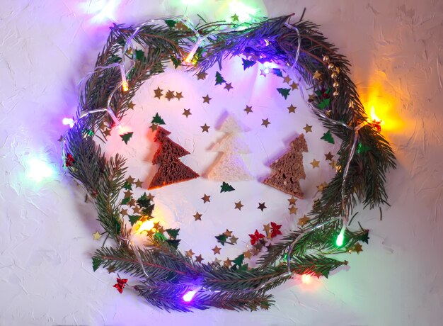 Sfondo festivo di Natale o Capodanno. Composizione per biglietti di auguri con ghirlanda verde, ghirlande luminose colorate, brillantini e abeti fatti di pane. Concetto di vacanze.