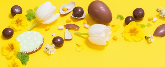 Sfondo giallo di Pasqua con uova di cioccolato, caramelle e spri