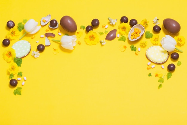 Sfondo giallo di Pasqua con uova di cioccolato, caramelle e spri