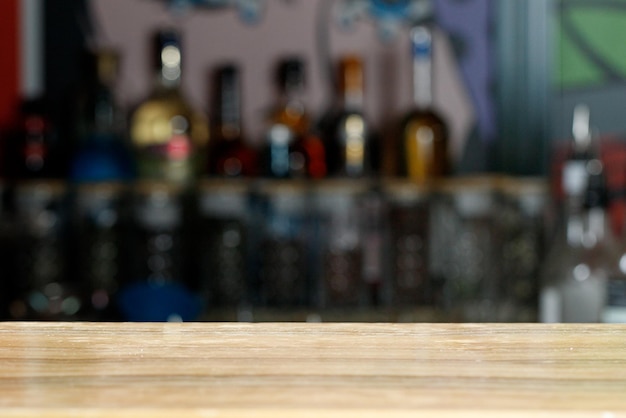 Sfondo moderno con tavolo in legno vuoto o bancone bar con bottiglie di alcol sfocate birra dietro