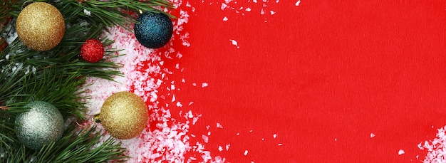 Sfondo natalizio con rami di abete neve artificiale e palle di Natale su carta ondulata rossa vista dall'alto Sfondo festivo per striscioni