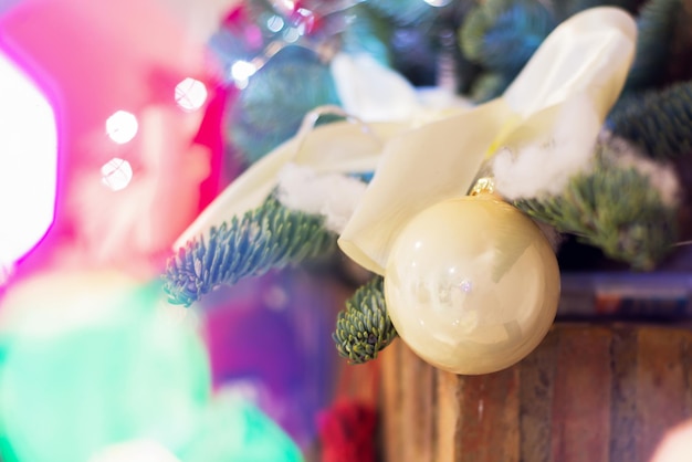 Sfondo natalizio di punti salienti sfocati dalle luci di una ghirlanda luminosa rami di un albero di Natale e una palla di vetro in primo piano a fuoco
