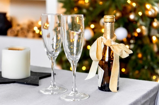 Sfondo natalizio festivo Accogliente serata a casa Due bicchieri e una bottiglia di champagne sullo sfondo di un albero di Natale e bokeh di ghirlande