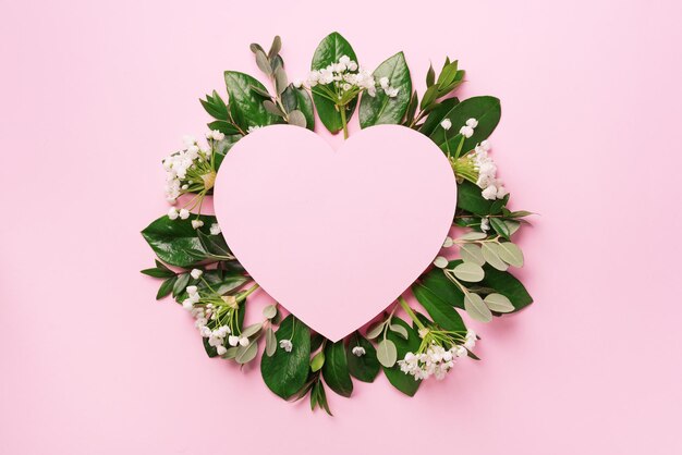 Sfondo natura tropicale con foglie verdi fiori bianchi e carta a forma di cuore rosa per lo spazio della copia Vista dall'alto Disposizione piatta Pubblicità creativa Estate e concetto di amore
