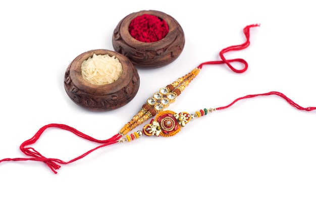 Sfondo Raksha Bandhan con un elegante Rakhi, chicchi di riso e Kumkum su sfondo bianco