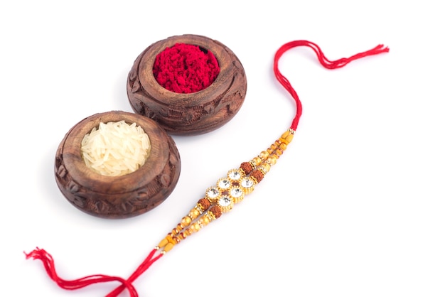 Sfondo Raksha Bandhan con un elegante Rakhi, chicchi di riso e Kumkum su sfondo bianco