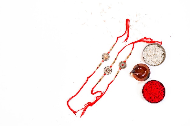 Sfondo Raksha Bandhan con un elegante Rakhi, chicchi di riso e Kumkum su sfondo bianco