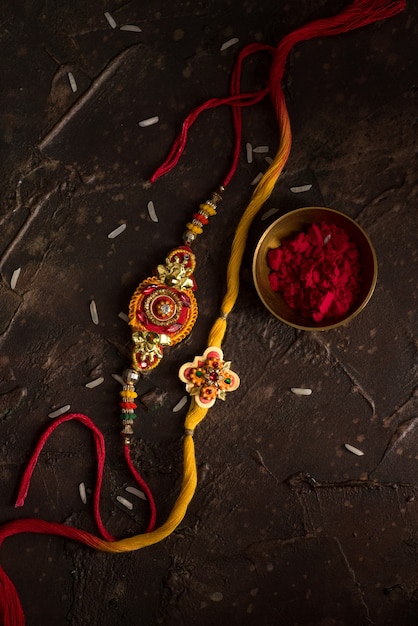 Sfondo Raksha Bandhan con un elegante Rakhi, Chicchi di Riso e Kumkum