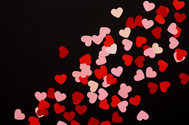 Sfondo romantico di San Valentino. Cuori di carta rosa e rosso su sfondo nero, vista dall'alto, copia spazio