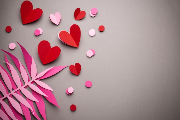 Sfondo romantico di San Valentino piatto, decorazione artistica di carta. Cuori di carta e foglie esotiche tropicali su sfondo grigio neutro. Origami del mestiere di concetto di celebrazione di San Valentino, spazio per testo