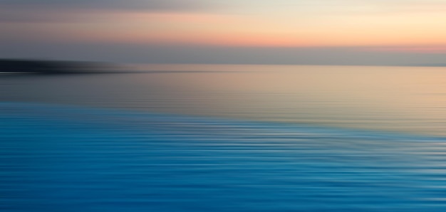 Sfondo sfocato di rifrazione in acqua. Vista panoramica drammatica della Piscina a sfioro con tramonto sul mare al crepuscolo.