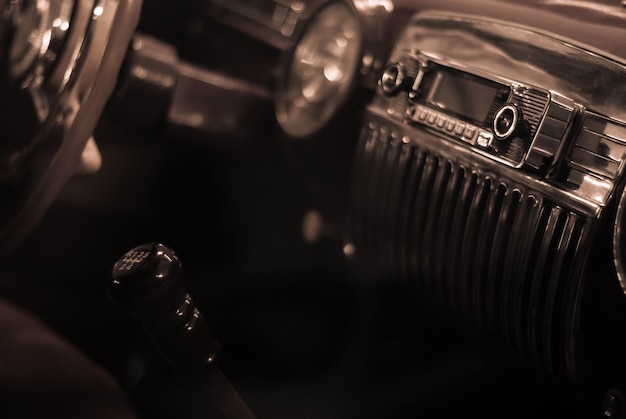 Sfondo sfocato stilizzato come una vecchia foto monocromatica: un frammento dell'interno di un'auto d'epoca, messa a fuoco sulla maniglia della radio