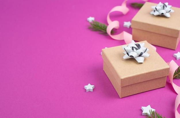 Sfondo vacanze di Natale con piccole scatole regalo, stelle e rami di abete, sfondo rosa alla moda