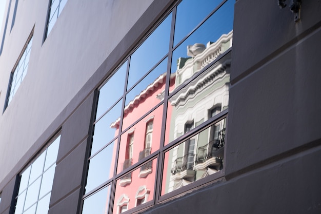 Sfondo vetroso della costruzione di un muro di cemento grigio con vetro riflesso sulla finestra che riflette il cielo blu e le case all'aperto