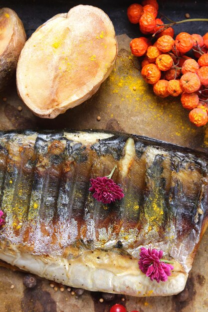 Sgombro alla griglia con spicchi di patate al forno bacche e fiori rosa su carta pergamena Concetto di cibo sano Primo piano