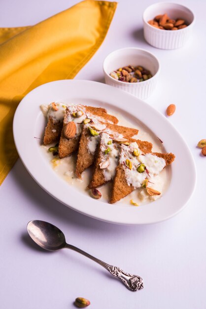 Shahi tukda o Double ka meetha è un budino di pane nel burro chiarificato, guarnito con latte condensato, noci e Mawa/khoya. Popolare dessert indiano, servito in un piatto su sfondo lunatico. Messa a fuoco selettiva