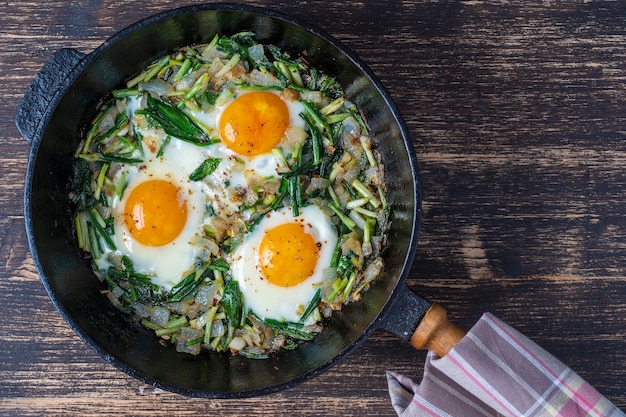 Shakshuka, uova fritte con foglie di aglio selvatico verde, cipolla, pepe e spezie in padella in ghisa, primo piano. Uova fritte con aglio selvatico come shakshuka