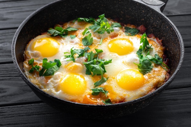 Shakshuka uova in una padella su uno sfondo di legno nero uova in camicia in un pomodoro piccante e peppe