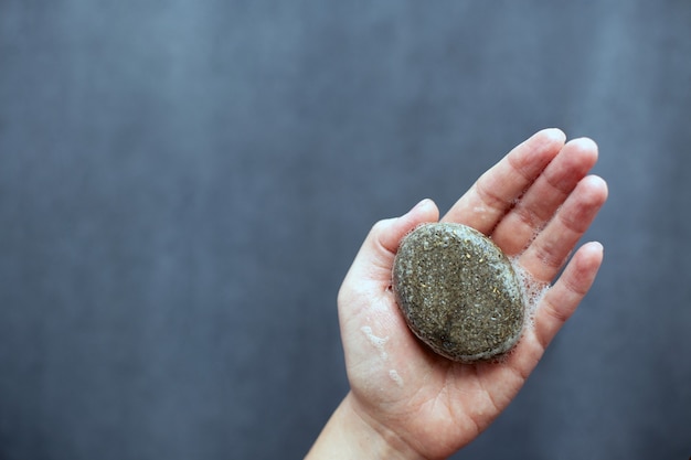 Shampoo bar naturale all'ortica solido tenuto dalla mano femminile. Concetto di rifiuti zero. Scelta di prodotti ecologici senza plastica. Sfondo grigio, copia dello spazio