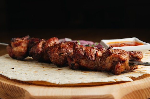 Shashlik russo tradizionale su uno spiedino di barbecue con cipolla, lavash e salsa su tavola di legno