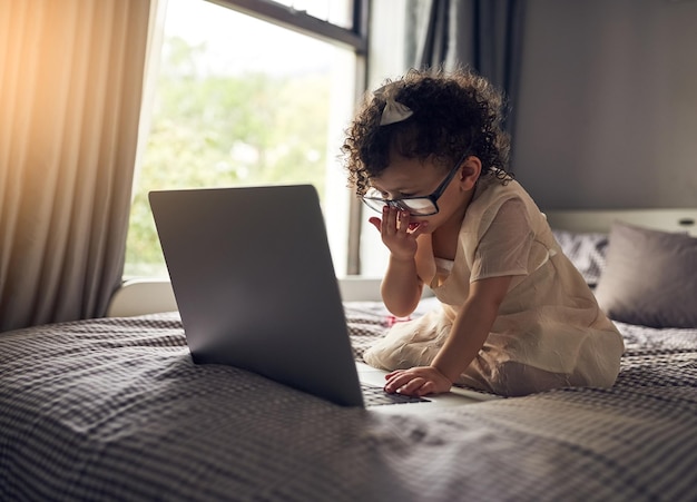 Shes techsavvy Foto a figura intera di un'adorabile bambina che usa un laptop mentre è seduta su un letto