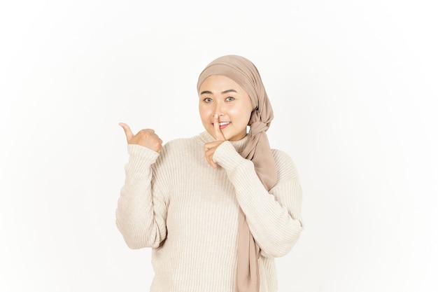 Shh e indicando da parte della bella donna asiatica che indossa l'hijab isolato su sfondo bianco