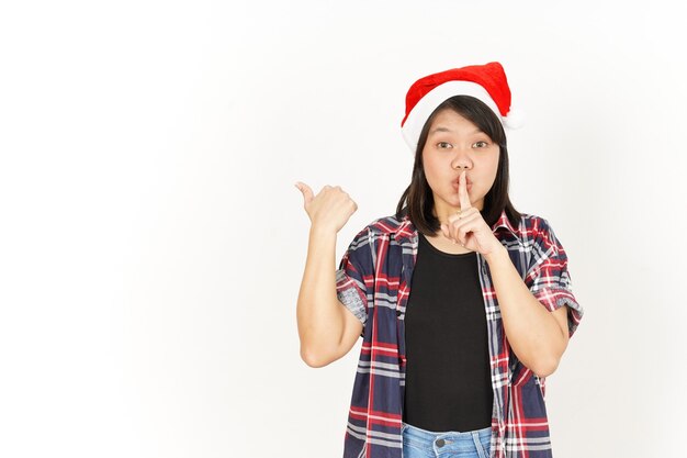 Shh e prodotto di puntamento a sinistra di una bella donna asiatica che indossa una camicia scozzese rossa e un cappello da Babbo Natale