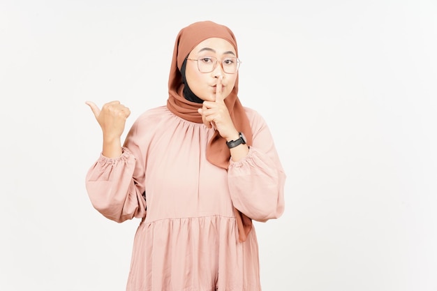 Shh gesto che presenta e indica il prodotto laterale utilizzando il pollice della bella donna asiatica che indossa l'hijab