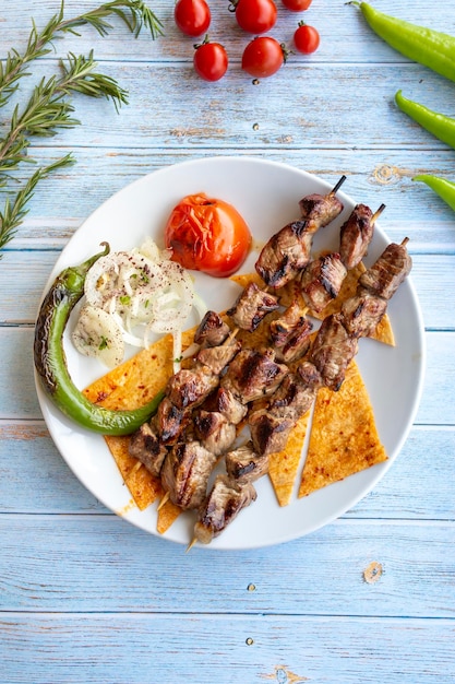 Shish kebab di agnello su fondo di legno blu con pomodori arrostiti, cipolle e peperoni