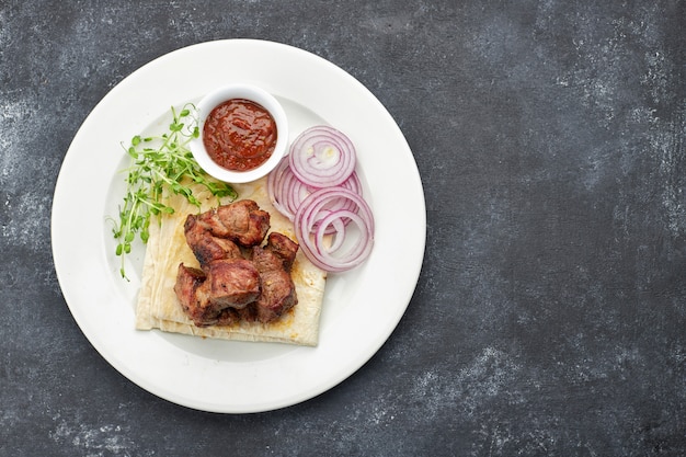 Shish kebab fritto con lavash, salsa, microgreen e cipolla su un piatto bianco su grigio