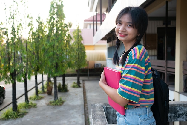 Shool ragazza tenere libro con backpak in piedi al campus