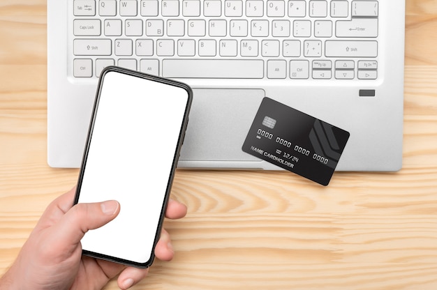 Shopping a pagamento online, pagamento elettronico con carta di credito. man mano che tiene il telefono cellulare intelligente, utilizzando la carta di credito per lo shopping online con il computer portatile