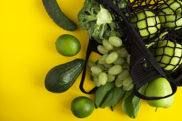 Shopping bag in rete nera con frutta e verdura verde su giallo