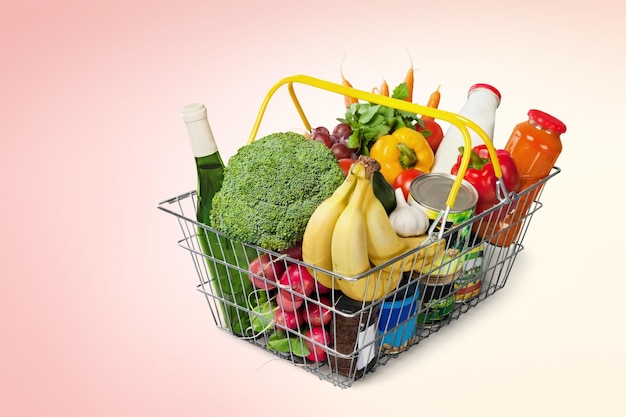 shopping basket with different groceries on pastel background