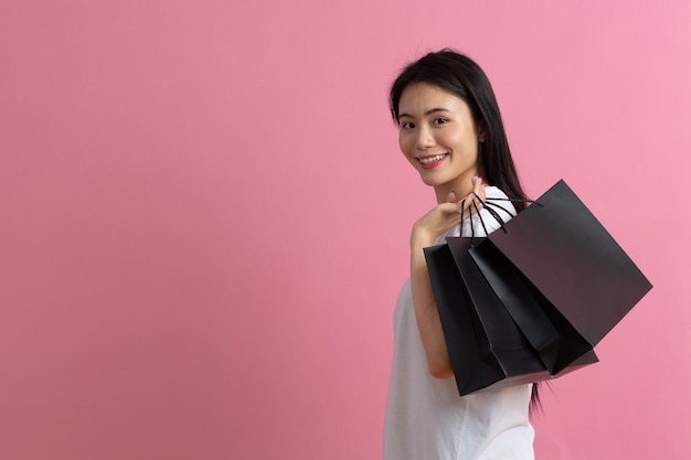 Shopping donna felice asiatica che tiene le borse della spesa su sfondo rosa