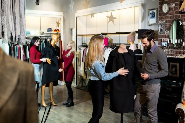 Shopping, moda, vestiti, stile e concetto di persone: amici felici che provano il cappotto in un centro commerciale o in un negozio di abbigliamento