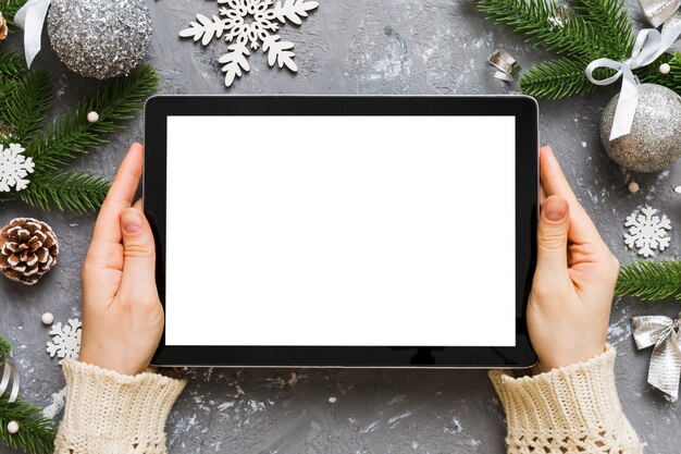 Shopping online di Natale da casa mani femminili che tengono tablet PC con schermo bianco vuoto vista superiore donna che tiene tablet con schermo vuoto albero di Natale e regali sullo sfondo