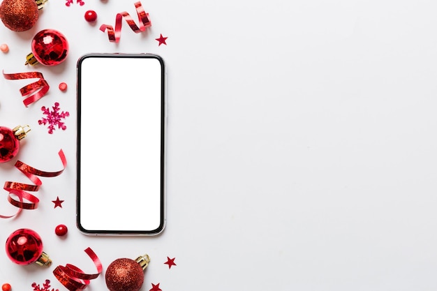 Shopping online di Natale da casa telefono con display bianco vuoto vista superiore smart mobile con spazio di copia su sfondo colorato con decorazioni natalizie palle sfondo di vendite per le vacanze invernali