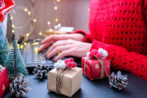 Shopping online di Natale, lavoro e istruzione. Decorazioni di Capodanno sul tavolo. Donna con computer portatile a casa. Saldi vacanze invernali. Confezioni regalo, alberi di Natale. Luce ghirlanda