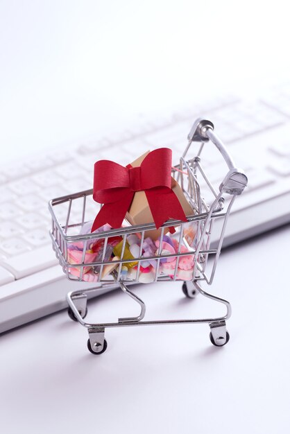 Shopping online e concetto di e-commerce foto con un carrello della spesa pieno di scatole regalo tagliate carta contro la tastiera.